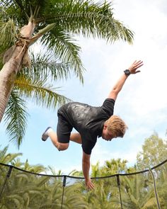 a young man is doing a trick on a trampoline in front of palm trees