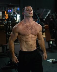 a man without a shirt standing in a gym with his eyes closed and no shirt on