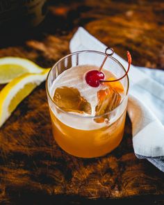 a drink with a cherry garnish on the top and lemon wedges next to it