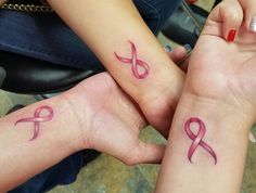 two women with matching pink tattoos on their arms holding hands in the shape of a heart