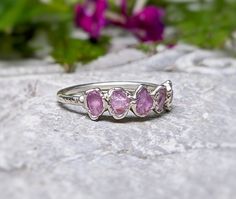 three stone ring sitting on top of a rock with flowers in the backgroud