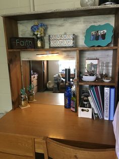 a wooden desk with books and vases on it next to a wall mounted mirror