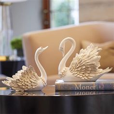 two white swans sitting on top of a table next to a book and glass vase