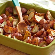 a green casserole dish with potatoes and a wooden spatula in it on a table