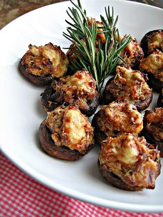 a white plate topped with stuffed mushrooms covered in cheese and seasoning next to a sprig of rosemary