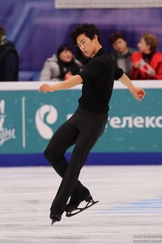 a man skating on an ice rink while people watch from the sidelines behind him