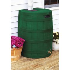 a large green barrel sitting on top of a wooden floor next to potted plants