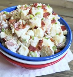 a blue bowl filled with potato salad on top of a wooden table next to a white and red napkin