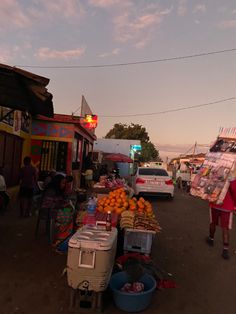 a woman walking down a street next to a fruit stand