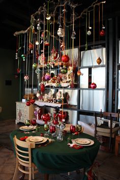 the table is set for christmas dinner with ornaments hanging from the ceiling and plates on it