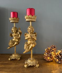 two golden candlesticks sitting on top of a wooden table next to a pine cone