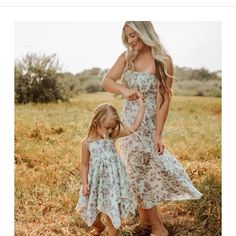 a mother and daughter standing in a field together, both wearing dresses with flowers on them