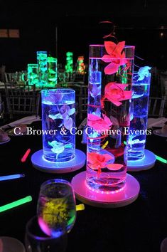 three tall vases with flowers in them are lit up by colored lights at an event