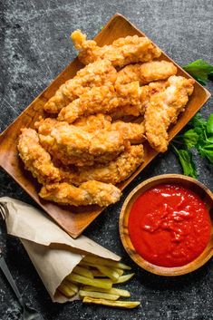 fried chicken with ketchup and french fries on a cutting board next to a bowl of sauce