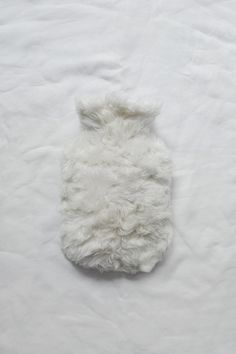 a white furry dog coat laying on top of a bed next to a stuffed animal