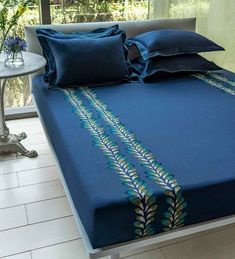 a bed with blue sheets and pillows on top of it next to a white table