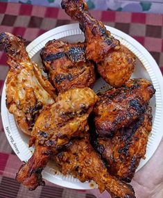 a person holding a paper plate with chicken wings on it