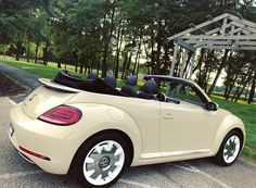 a beige convertible car parked in a parking lot next to some trees and grass with the top down