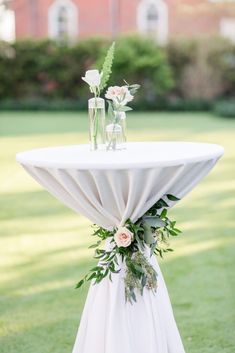 a white table with flowers and greenery on it in the middle of a field