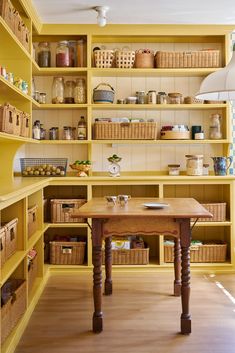 a kitchen with yellow shelving and lots of baskets on the shelf above the table