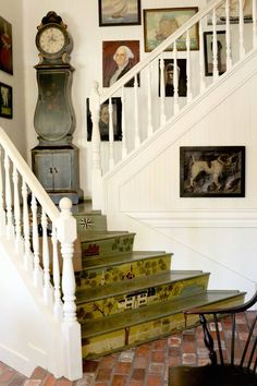 there is a clock on the wall next to some stairs in this house with pictures all over it