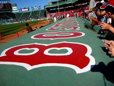 some people are writing on the ground at a baseball game with red and white numbers