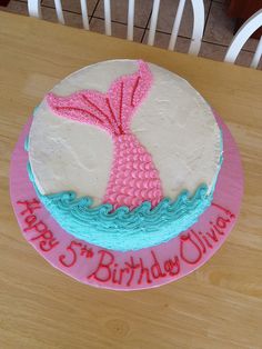 a birthday cake decorated with a pink and blue mermaid tail sitting on top of a wooden table