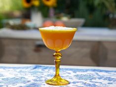 an orange drink sitting on top of a blue and white tablecloth with flowers in the background