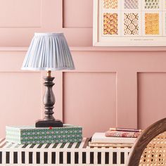 a lamp sitting on top of a wooden table next to a chair and pink wall