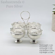 two silver bowls sitting on top of each other next to a potted green plant