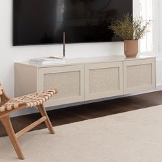 a flat screen tv mounted on the wall above a white entertainment center with wicker chairs