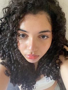 a close up of a person with curly hair wearing a tank top and looking at the camera