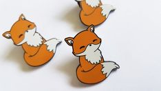 three pin badges depicting two red foxes and one white fox, on a white background