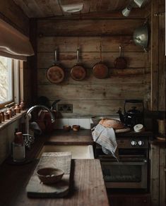 a rustic kitchen with wooden walls and counter tops, pots and pans hanging on the wall