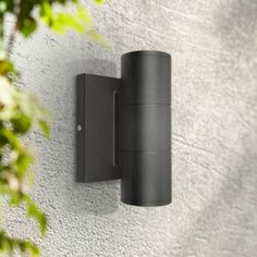 an outdoor light mounted on the side of a wall next to a tree and bushes