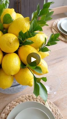 a bowl full of lemons sitting on top of a wooden table next to plates