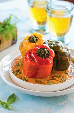 a white plate topped with stuffed peppers next to two glasses of orange juice and bread