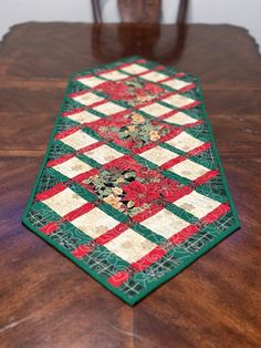 a wooden table topped with a green and red patchwork quilted placemat on top of a wooden table