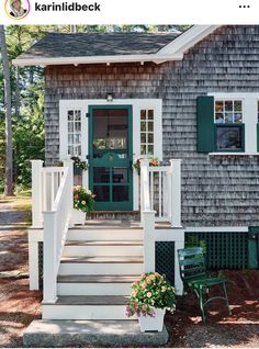 a small gray house with green shutters on the front door and steps leading up to it