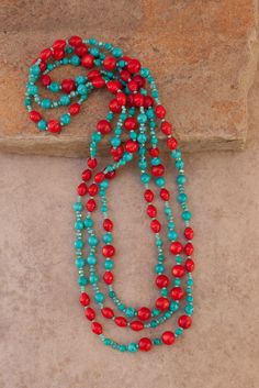 a long beaded necklace with red and turquoise beads on a stone slab next to a rock