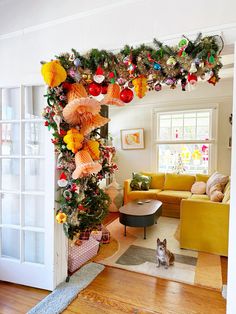 a living room decorated for christmas with decorations on the tree and cat sitting under it