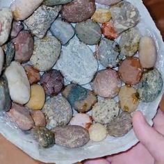 a bowl filled with lots of rocks on top of a wooden table next to a person's hand