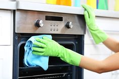 a woman cleaning an oven with a blue towel and green gloves on her hand,