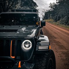 a black jeep parked on the side of a dirt road next to trees and bushes