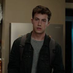 a young man standing in front of a refrigerator freezer wearing a backpack and looking at the camera