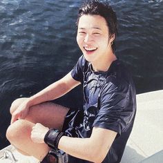 a young man sitting on top of a boat next to the ocean with his camera