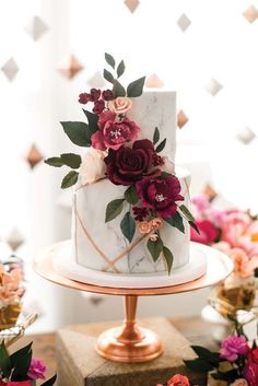 a white and gold wedding cake with red flowers on the top is sitting on a table