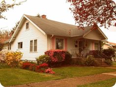 a white house with red flowers in the front yard and green grass on both sides