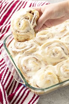 a person holding a cinnamon roll in a glass baking dish