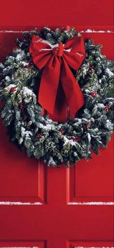 a christmas wreath on a red door with a bow hanging from the front and side